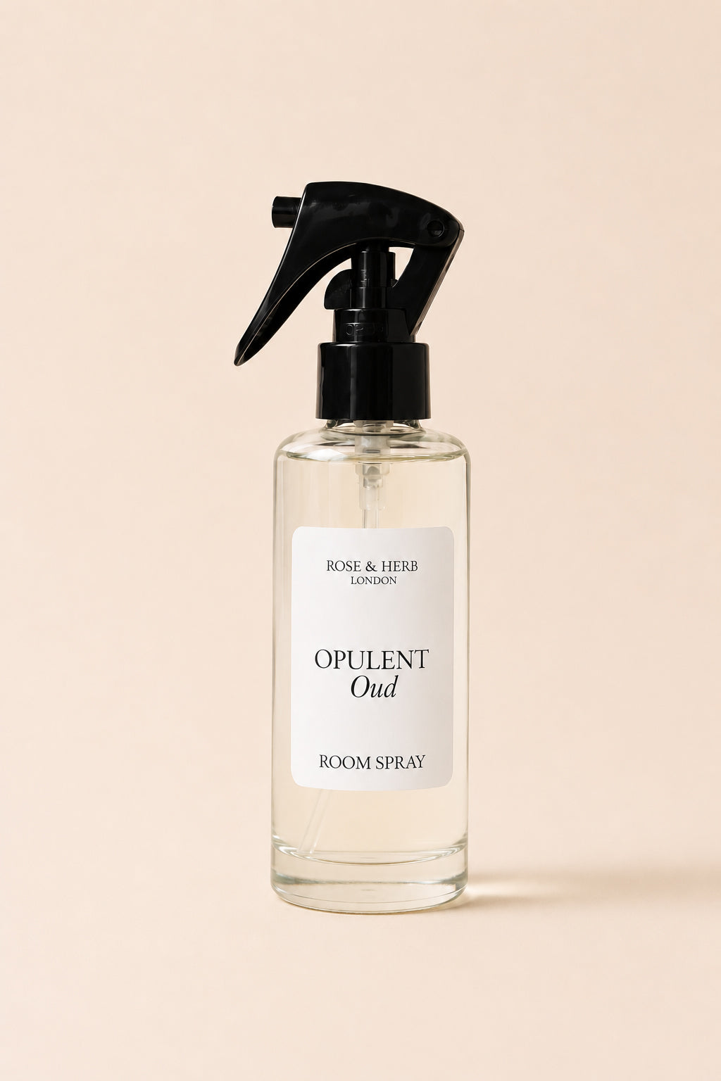 A clear glass room spray bottle with a black trigger sprayer and a white label reading 'OPULENT Oud' and 'ROSE & HERB LONDON', centered on a warm beige background.