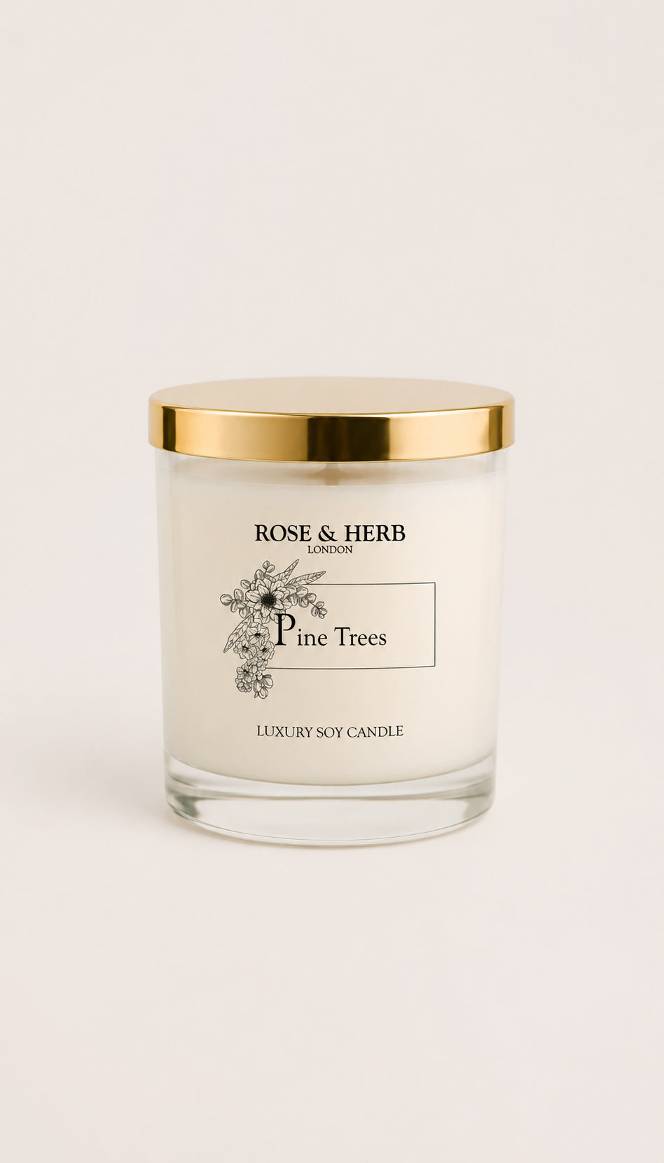 A Rose & Herb London 'Pine Trees' luxury soy candle in a clear glass jar with a shiny gold lid, set against a clean, light beige background.