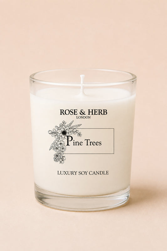 A single-wick luxury soy candle in a clear glass jar with white wax, featuring a black printed label that reads 'ROSE & HERB LONDON', 'Pine Trees', and 'LUXURY SOY CANDLE' on a soft beige background.