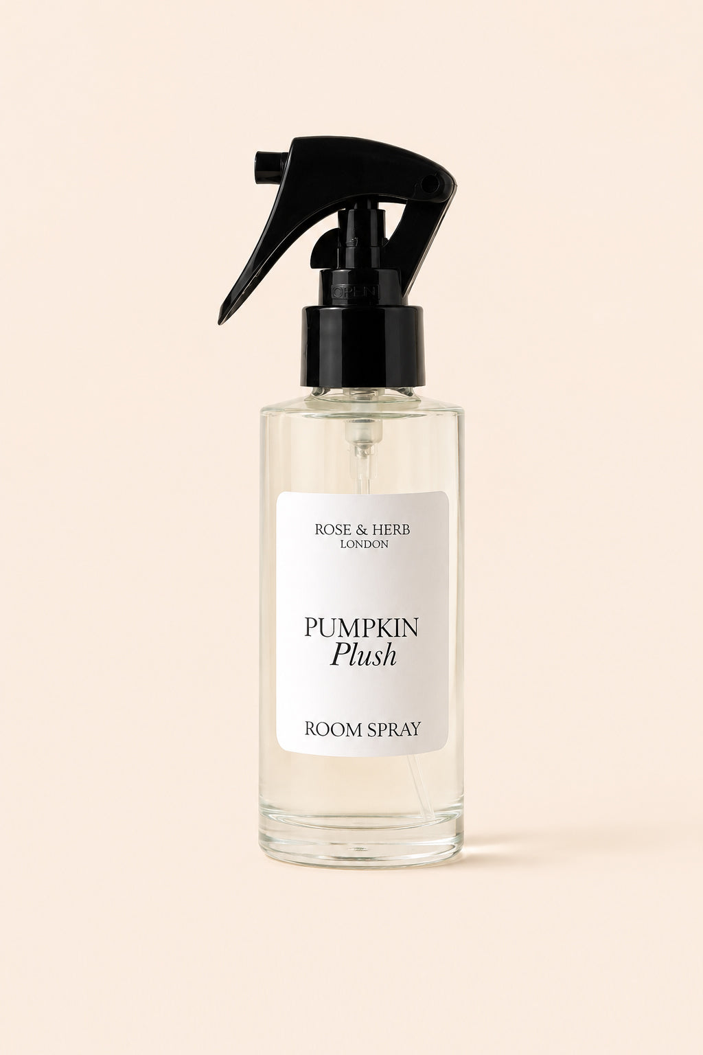 A clear glass room spray bottle with a black trigger spray top and a white label reading 'Rose & Herb London Pumpkin Plush Room Spray', centered on a warm beige background.