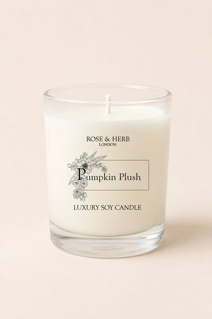 A single-wick luxury soy candle in a clear glass jar with white wax, labeled 'Pumpkin Plush' by Rose & Herb London, set against a solid pale pink background.